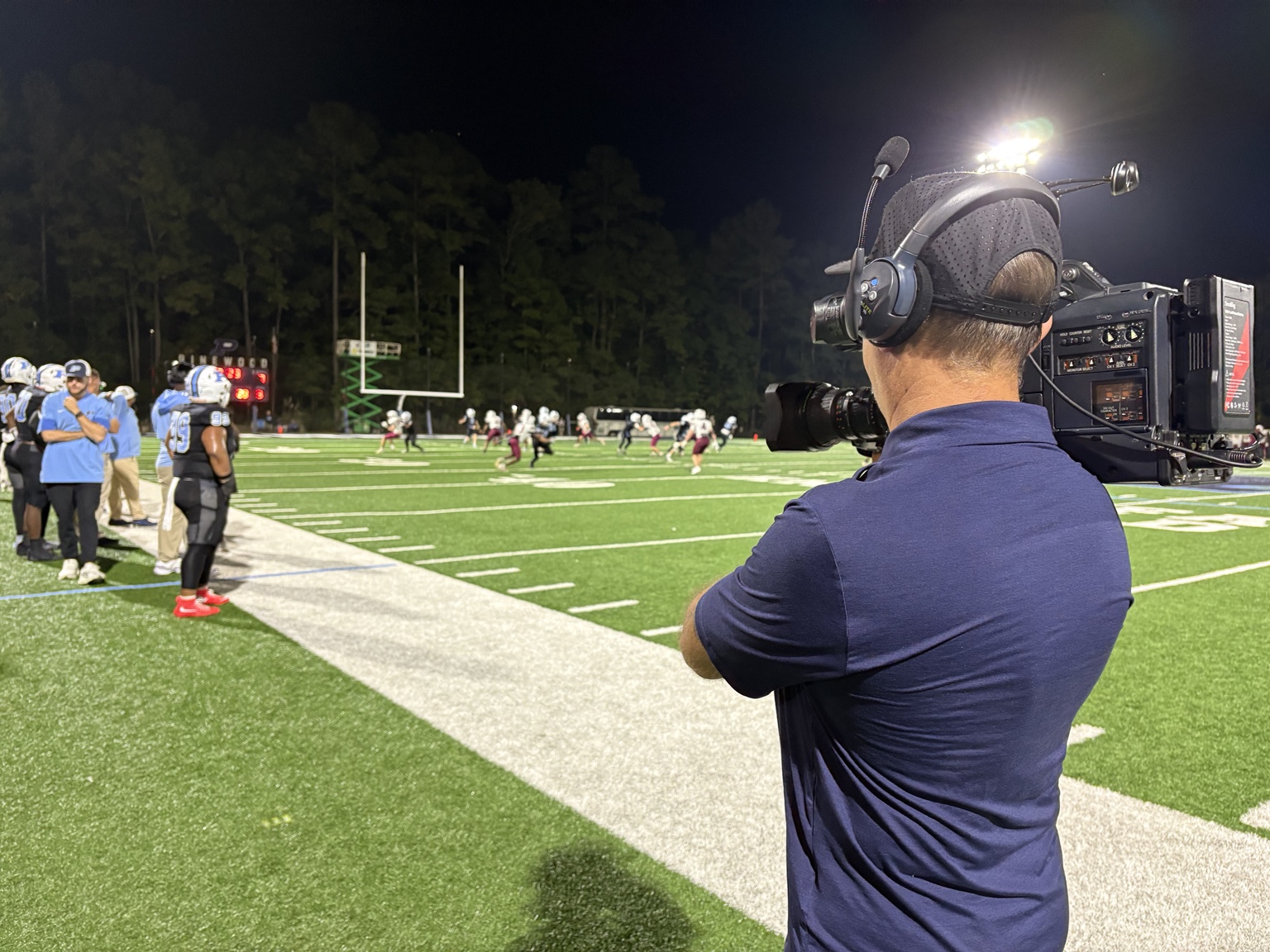 Sergio Myers filming live high school football from the sideline as players compete downfield
