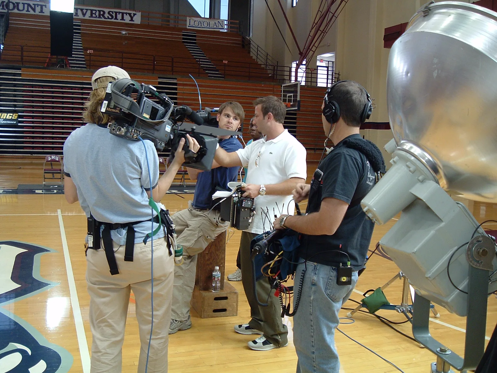 Camera, audio, and production crew preparing broadcast coverage inside a university gymnasium